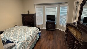 A bedroom with a bed, dresser, vanity, and a ceiling fan.