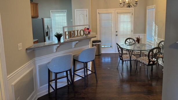 A modern kitchen with a built-in island, a dining area with a glass table and chairs, and a chandelier.