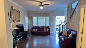 A spacious living room with hardwood flooring, a ceiling fan, and two leather sofas with cushions.