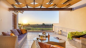 A sunlit balcony with wicker furniture, a glass table, and a view of a distant landscape. - Hg07 Adjacent to Aphrodite Hills- Private Pool, Large Terrace (Kouklia)