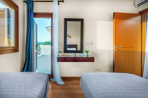 A bedroom with two beds, a wooden door, a mirror, a small shelf with a plant, and a window with curtains.