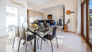 A modern living room with a glass dining table, black chairs, a stone accent wall, and a large window. - Hg07 Adjacent to Aphrodite Hills- Private Pool, Large Terrace (Kouklia)