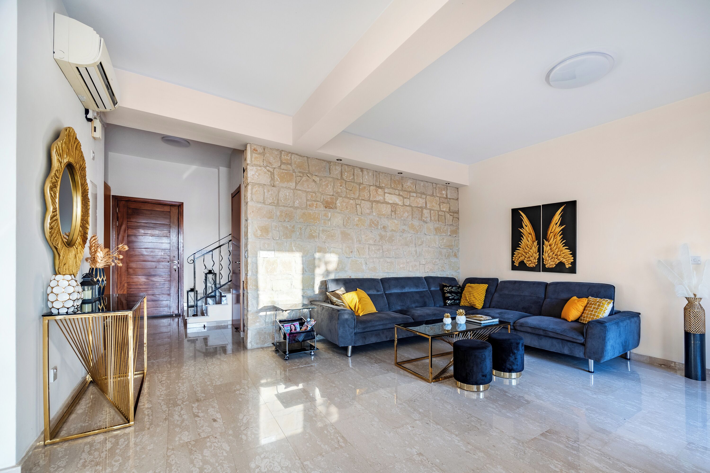 A modern living room with a stone accent wall, a blue sofa set, and a gold-framed console table.