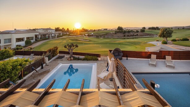 A pool area with two swimming pools, a sun terrace with wooden loungers, and a view of a golf course at sunset. - Hg07 Adjacent to Aphrodite Hills- Private Pool, Large Terrace (Kouklia)