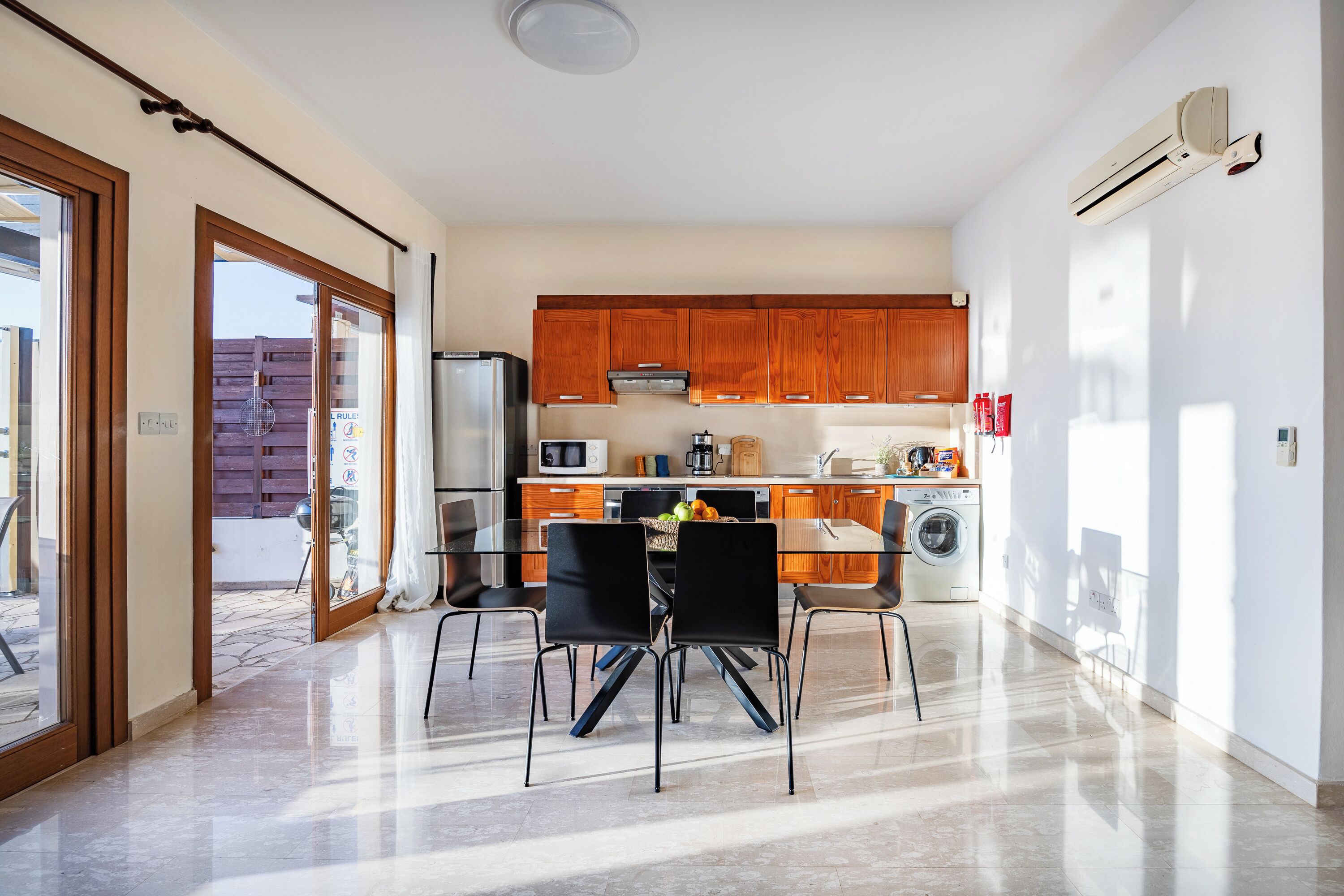 Een moderne keuken met houten kastjes, een roestvrijstalen koelkast en een eethoek met een glazen tafel en zwarte stoelen.