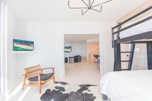 A modern bedroom with a bunk bed, a wooden chair, a cowhide rug, and a television displaying a beach scene.