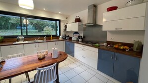 A modern kitchen with a wooden table, white and blue cabinets, a gas stove, and a window overlooking greenery. - Large family home (Combrit)