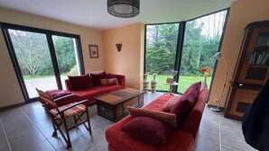 A spacious living room with a red sofa, a wooden coffee table, and a dining area with chairs. Large windows offer a view of the outdoors. - Large family home (Combrit)