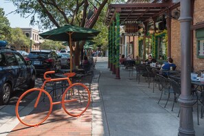 A street with outdoor seating at a restaurant, a bicycle, and parked cars.