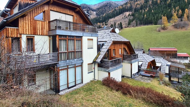 Un moderno chalet con un balcón grande, fachada de madera y vistas a un paisaje montañoso.