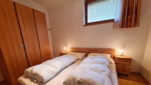 Un dormitorio con una cama de madera, dos mesitas de noche con lámparas, un armario y una ventana con persianas.