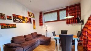 Una sala de estar con un sofá marrón, una mesa de comedor con sillas, una lámpara y obras de arte en las paredes.