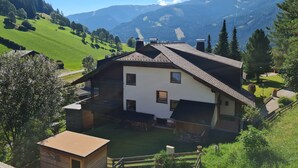 Una casa de dos pisos con techo inclinado, rodeada de colinas y montañas verdes y exuberantes.