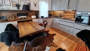 A modern kitchen with a wooden countertop, a black pendant light, and a dining area with a wooden table and chairs. - Apartment With Carinthian Mountain View (Bad Kleinkirchheim)