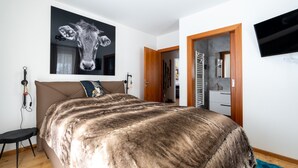 A bedroom with a large bed, a mounted TV, and a door leading to a bathroom. - Apartment With Carinthian Mountain View (Bad Kleinkirchheim)