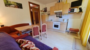 A compact living space with a sofa, a dining table, a kitchen area with a stove, microwave, and cabinets. - Beautiful Apartment in Bad Kleinkirchheim (Bad Kleinkirchheim)