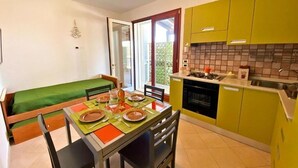 Une cuisine compacte avec des meubles de couleur verte, une table à manger pour quatre personnes et un petit coin repas agrémenté d’un chemin de table vert.
