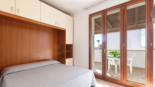 Une chambre à coucher comprenant un lit, une armoire en bois et une porte-fenêtre coulissante donnant sur un espace extérieur avec une table et des chaises.
