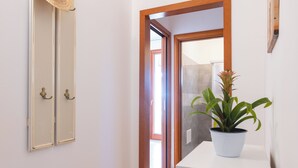 Un couloir avec une plante en pot, un miroir et une porte donnant sur une autre pièce.