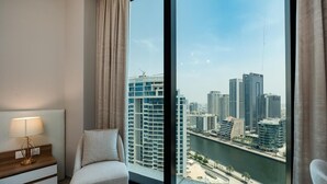 A modern hotel room with a large window offering a city view, a bed, a bedside table with a lamp, and a view of a river.