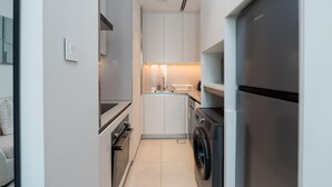 A compact kitchen with white cabinets, a washing machine, a refrigerator, and a countertop with a sink.