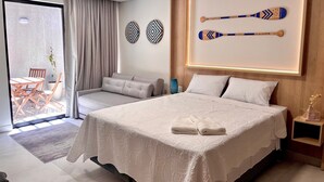 Una habitación de hotel moderna con una cama grande, un área de estar con un sofá y sillones, una mesa de comedor y vistas a través de una puerta corredera.