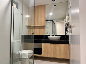 Ein modernes Badezimmer mit einer begehbaren Duschkabine aus Glas, einer weißen Toilette, einem schwarzen Waschbecken und Holzschränken.