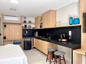 Eine kleine Küche mit Holdekor, einer schwarzen Arbeitsplatte und einem kleinen Kühlschrank. Zwei Hocker und eine Kaffeemaschine sind vorhanden.