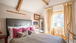 A bedroom with a large bed, a headboard, a bedside table with a lamp, a mirror, and a window with curtains. - Stunning contemporary cottage - The Bothy (Bibury)