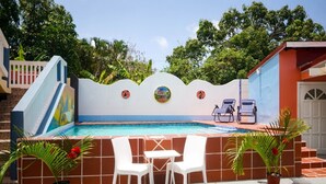Un espace piscine avec une terrasse carrelée, deux chaises blanches et une petite table.