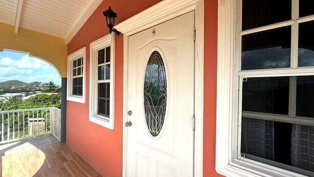 Une maison à l’extérieur rouge, avec une porte blanche dotée d’un vitrage et un balcon muni d’une balustrade.