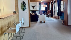 Un vaste espace de vie agrémenté d’un plafond en bois, d’une décoration murale représentant des cactus, d’un crâne de taureau accroché au mur et d’un coin salon confortable avec un canapé et des fauteuils.