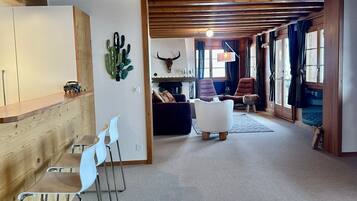 Ein geräumiger Wohnbereich mit Holzboden, einer Wanddekoration aus Kakteen, einem aufgehängten Bullenkopf und einer gemütlichen Sitzecke mit Sofa und Sesseln.