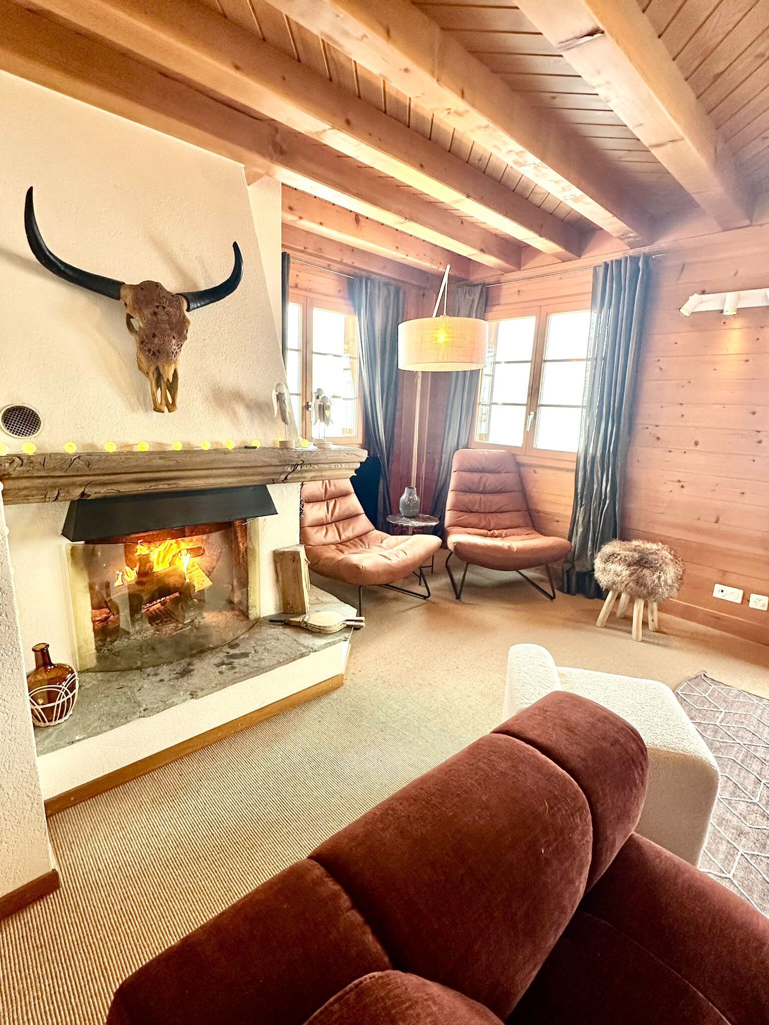 A cozy living room with a fireplace, leather chairs, a wooden ceiling, and a large bull skull decoration.