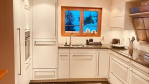 Une cuisine moderne avec des meubles blancs, une fenêtre offrant une belle vue et un plan de travail équipé de divers appareils électroménagers.