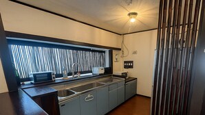 A kitchen with a built-in sink, a window with vertical blinds, and a light fixture on the ceiling. - NAGACHIBI (Miyakojima)