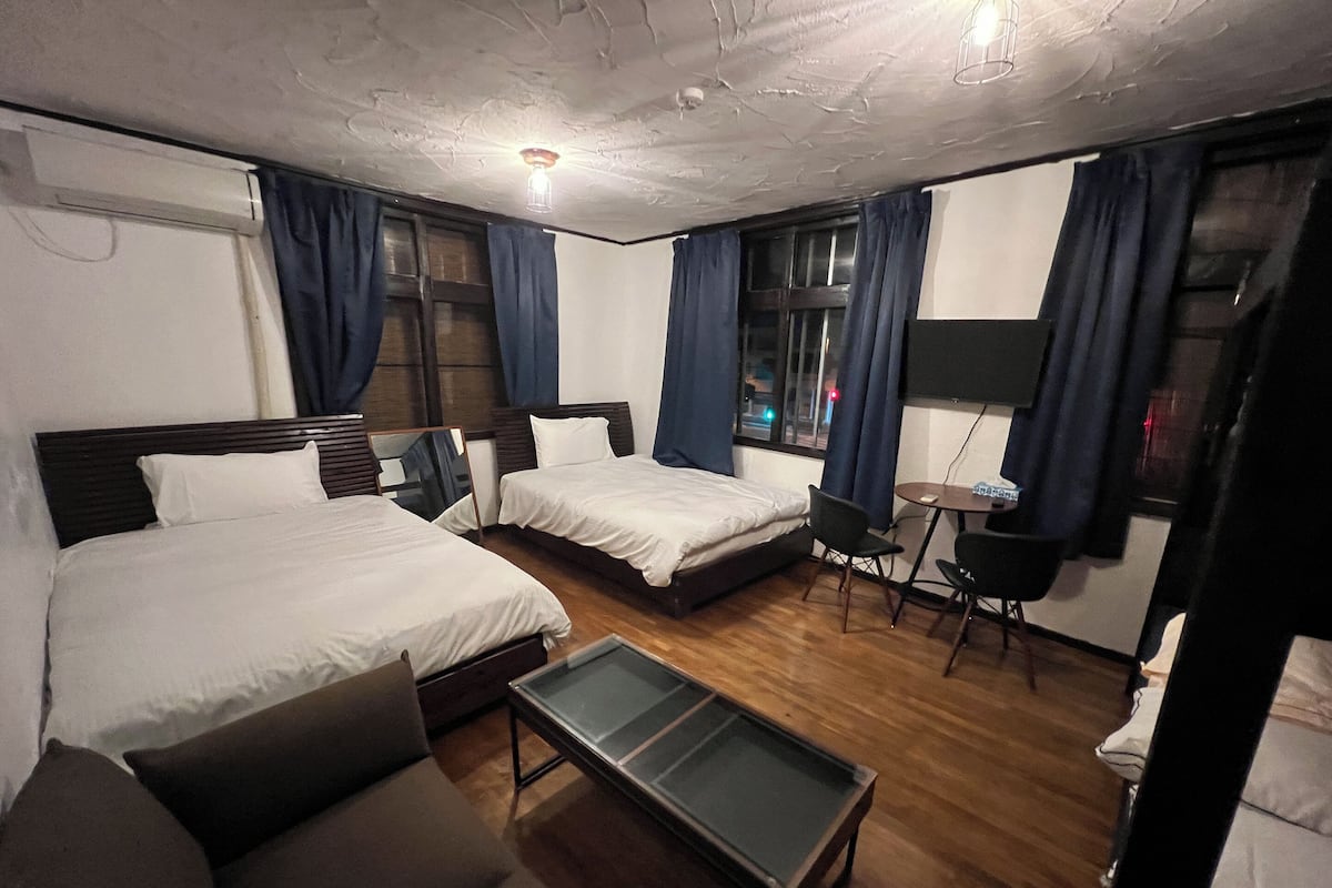 A hotel room with two beds, a small table, a sofa, and a desk with a chair.