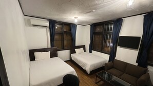 A hotel room with two single beds, a sofa, a small table, and an air conditioning unit. - NAGACHIBI (Miyakojima)