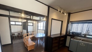 A compact kitchen with a dining area, wooden furniture, and a window with blinds. - NAGACHIBI (Miyakojima)