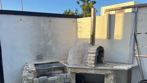 An outdoor brick oven structure with a chimney, surrounded by a concrete wall and a metal fence. - NAGACHIBI (Miyakojima)