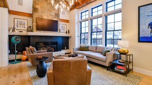 A cozy living room with a fireplace, a sofa, a coffee table, and a large window with a view.
