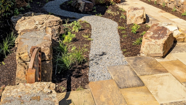 A landscaped garden with a stone pathway, a small water feature, and a house with a large garage and a covered patio.