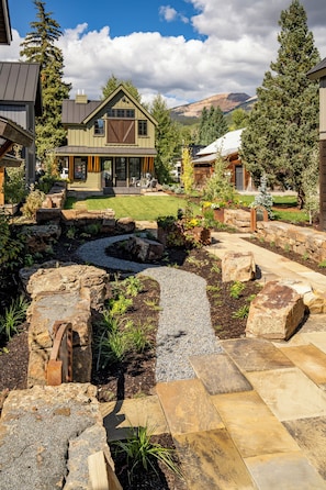 A landscaped garden with a stone pathway, a small water feature, and a house with a large garage and a covered patio.