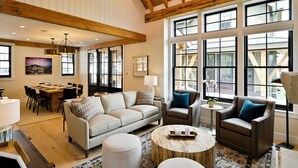 A spacious living room with a high ceiling, large windows, a dining area, and a cozy seating arrangement.