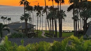 A beachfront property with a view of the ocean at sunset, palm trees, and a pathway leading to a building with a tiled roof. - Wailea Elua condo - Ocean Views | Gym | Pickleball (Wailea-Makena)