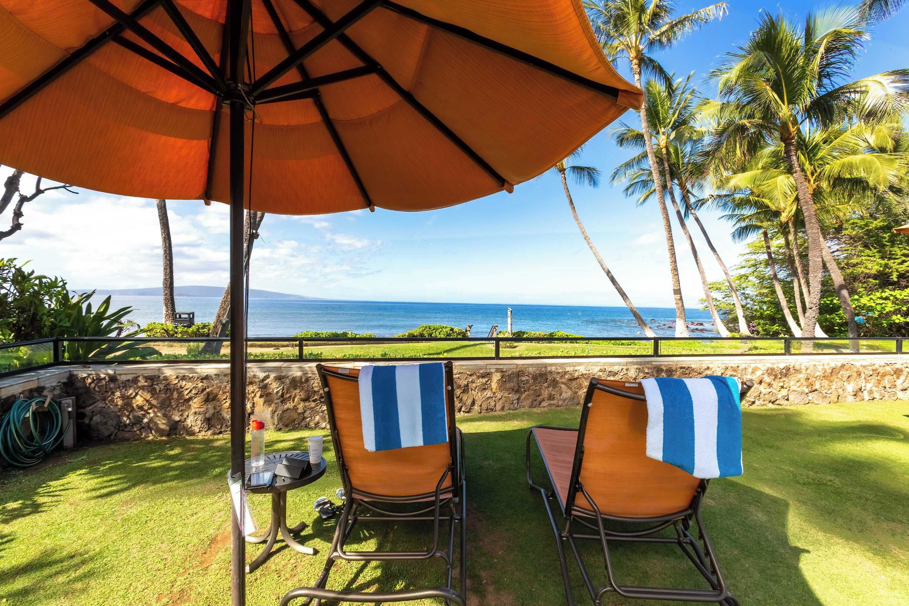 A patio with two chairs, an umbrella, and a view of the ocean.
