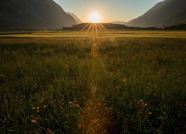 Un champ où le soleil se couche à l’horizon, entouré de montagnes.