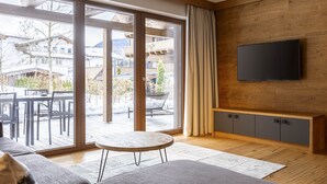 A modern living room with a large sliding glass door leading to an outdoor patio, a flat-screen TV mounted on the wall, and a wooden bench.