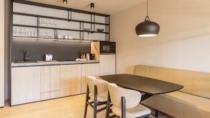 A modern kitchen with a dining area, featuring a built-in microwave, a coffee maker, and a shelf with glasses and bowls. - Lovely Apartment Near ski Area (Oberndorf in Tirol)