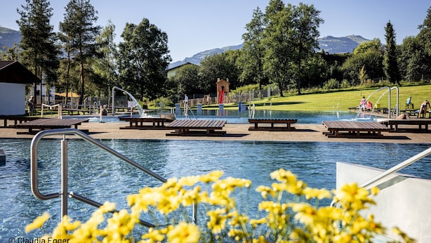 A swimming pool with wooden deck chairs, a small building, and a playground area. - Lovely Apartment Near ski Area (Oberndorf in Tirol)